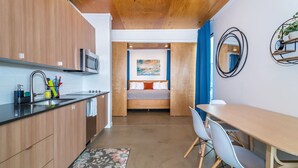 Une cuisine moderne avec des meubles en bois, un four à micro-ondes et un évier. On y trouve également un coin repas avec une table et des chaises, ainsi qu'un lit avec un tableau accroché au mur.