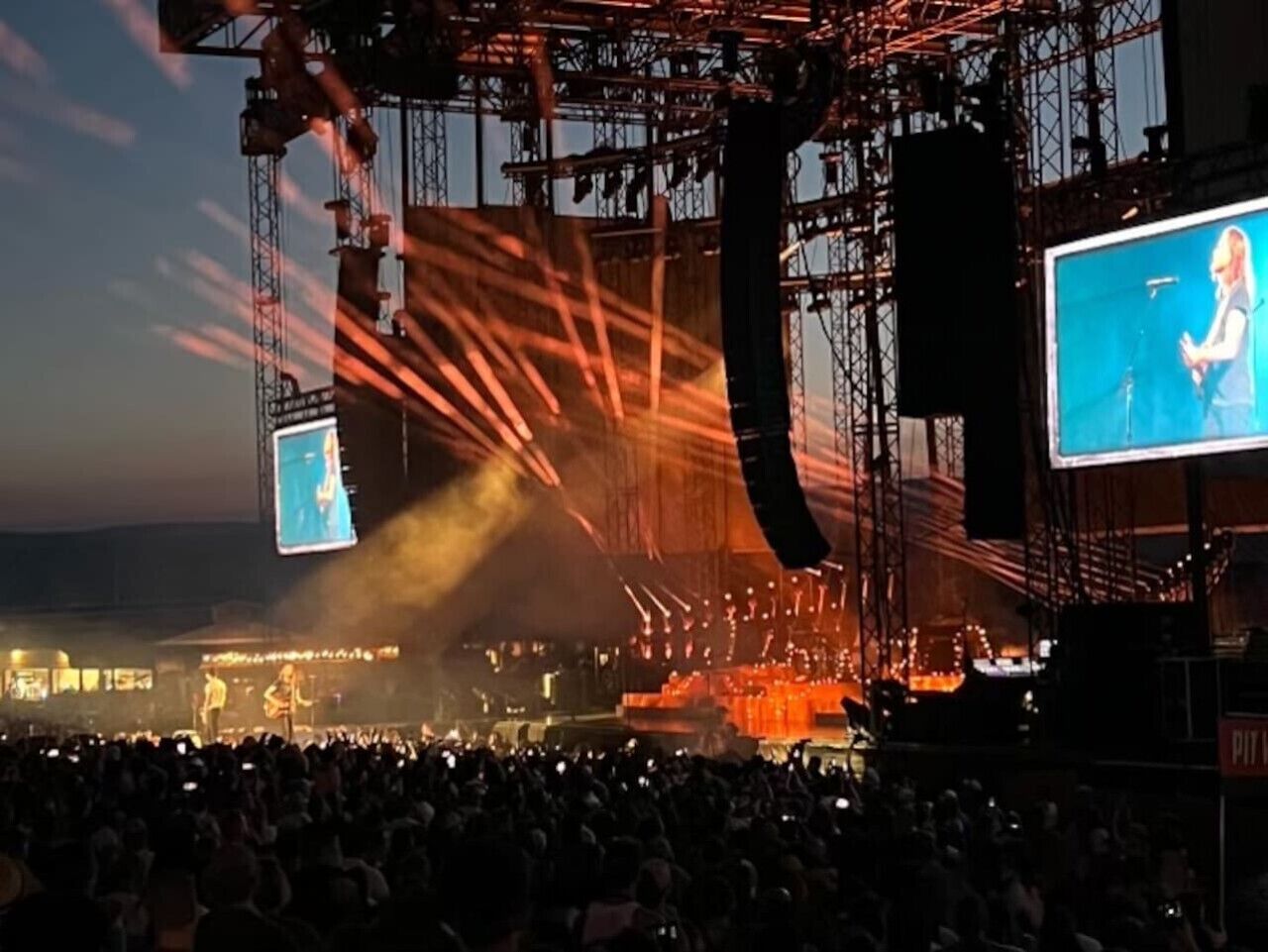 A concert stage with a large crowd and a complex lighting rig.
