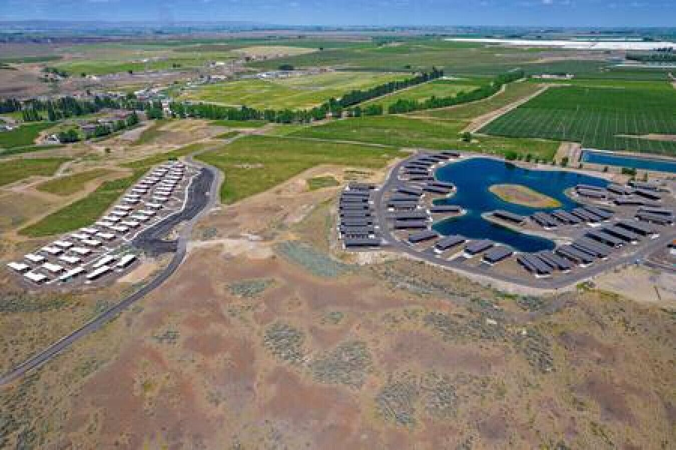 An aerial view of a campground with RV parking, a central lake, and surrounding fields.