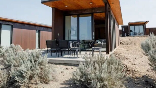 A modern building with a covered outdoor seating area, large windows, and a sandy landscape. - Wine Down in 3C at Cave B Ridge (Quincy)