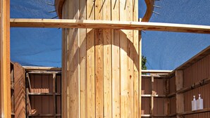 Una estructura cilíndrica de madera con una puerta, rodeada de muros de madera y un techo de lona azul.