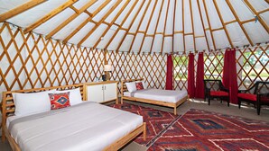 Una yurtar con dos camas, una mesita y cortinas rojas.