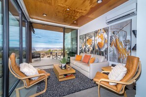 A modern living room with a large glass door leading to an outdoor patio, a white sofa, leather armchairs, and abstract wall art. - Cave B Ridge River View Retreat 3D - Wine & Relax (Quincy)