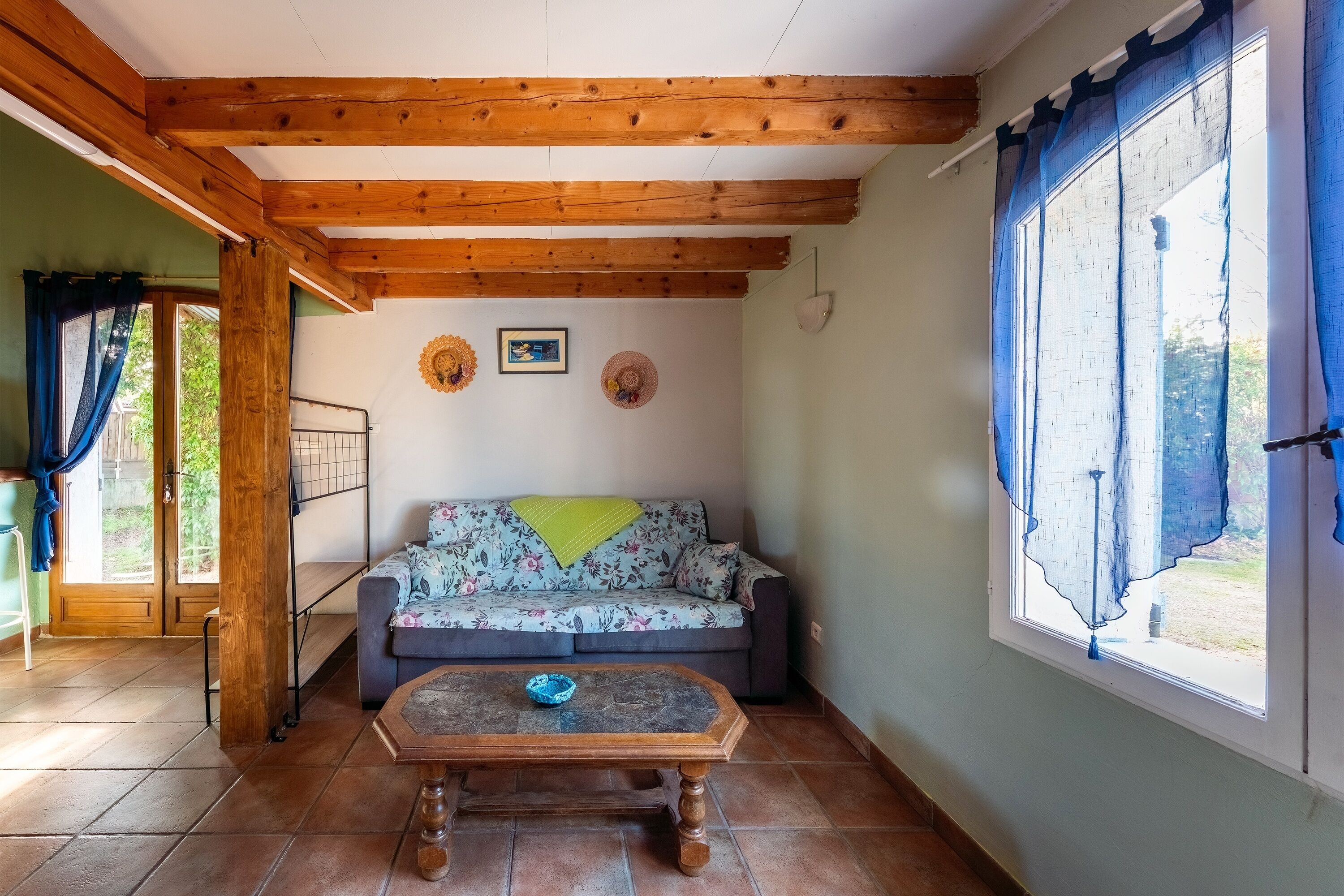 Una habitación acogedora con techo de madera, un sofá floral, una mesita y una ventana con cortinas.