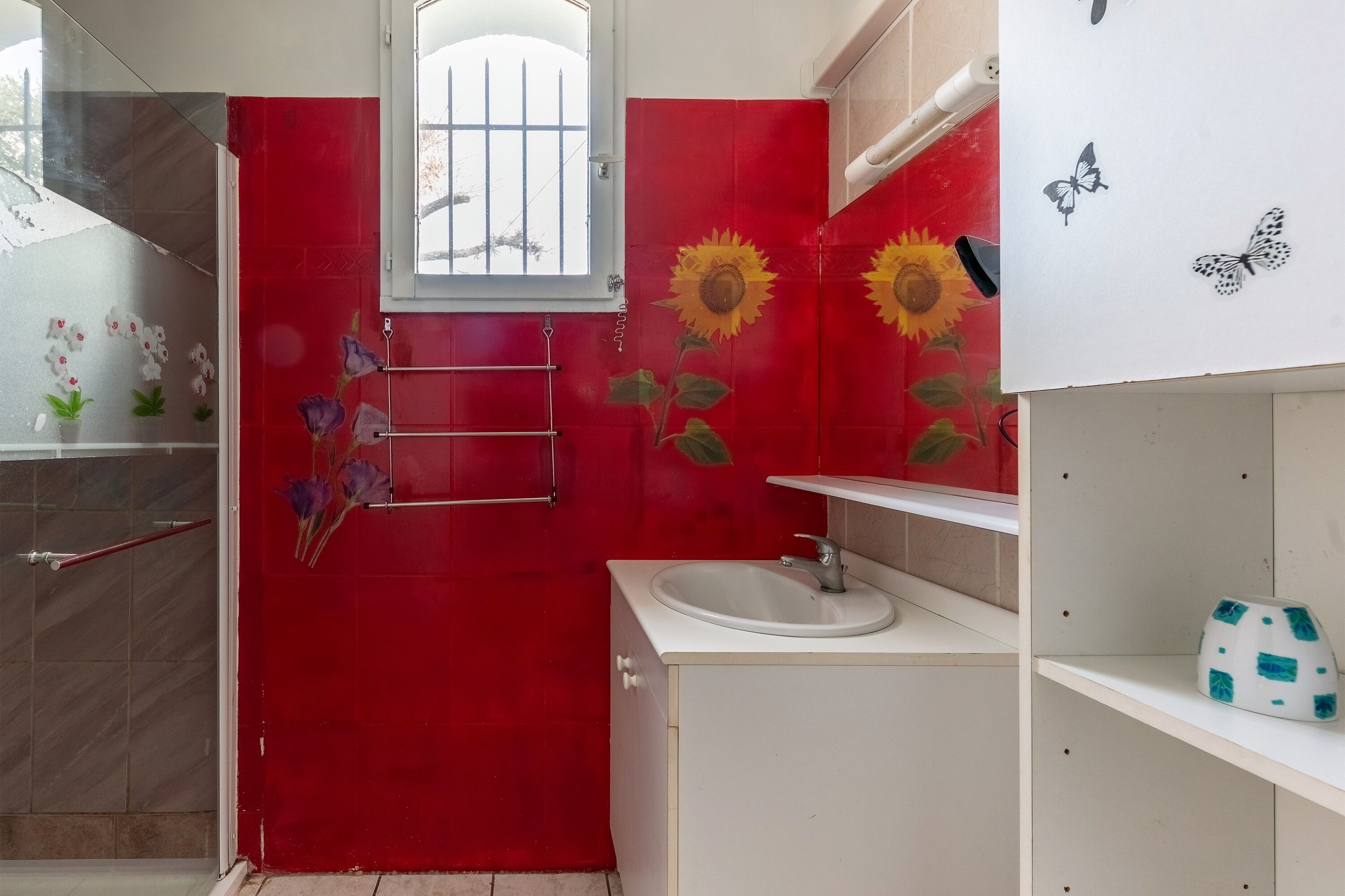 A bathroom with a red door, a window, a sink, and a shelf with a decorative item.