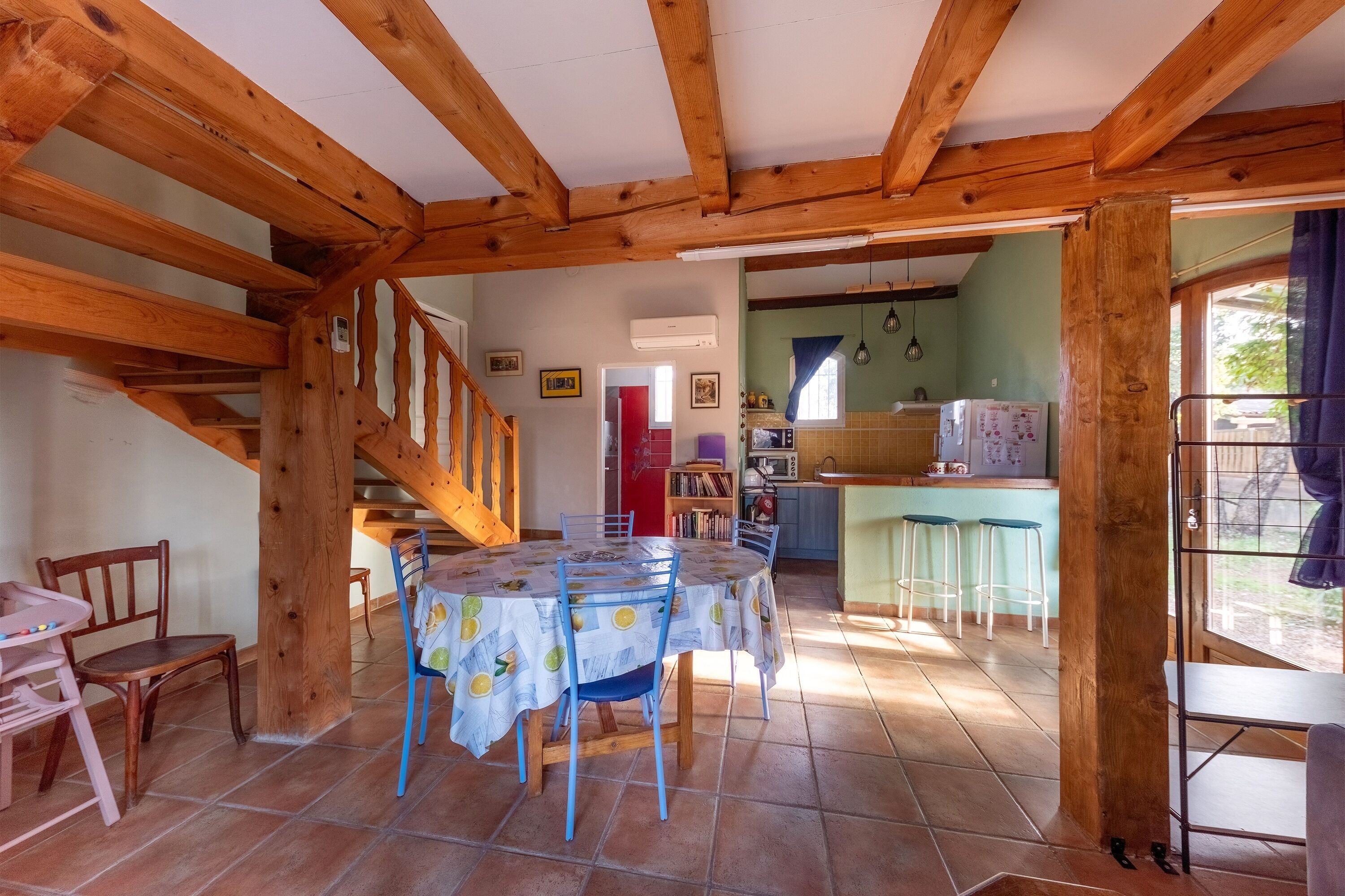 A rustic dining area with a wooden ceiling, a round table with chairs, and a kitchen in the background.