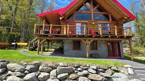 A wooden cabin with a red roof, a balcony, and a stone wall in front. - The Sugar Camp | Spa. Log cabin. Southern Massif. (Saint-Philémon)