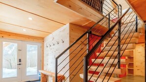 A wooden staircase with metal railings, a red accent wall, and a view of the outside through a glass door. - The Sugar Camp | Spa. Log cabin. Southern Massif. (Saint-Philémon)