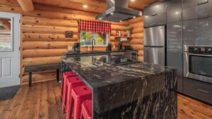 A log cabin kitchen with a central island, stainless steel appliances, and wooden walls. - The Sugar Camp | Spa. Log cabin. Southern Massif. (Saint-Philémon)