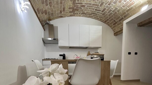 A modern kitchen with white cabinets, a wooden dining table, and chairs. There is a potted orchid on the table. - Double room with private bathroom and balcony (Spoltore)