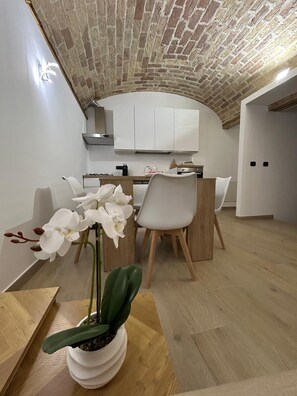 Une cuisine moderne avec des meubles blancs, une table à manger en bois et des chaises. On peut voir une orchidée en pot sur la table.
