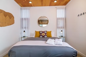 Um quarto moderno com uma cama grande, duas luminárias de cabeceira, um espelho redondo e uma peça de arte original na parede.