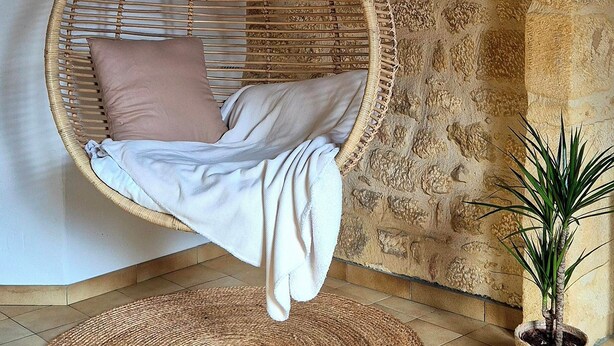 A wicker hanging chair with a cushion and a blanket, a woven rug on the floor, and a potted plant. - Cozy house in the heart of the Bastide with private courtyard and closed garage (Domme)
