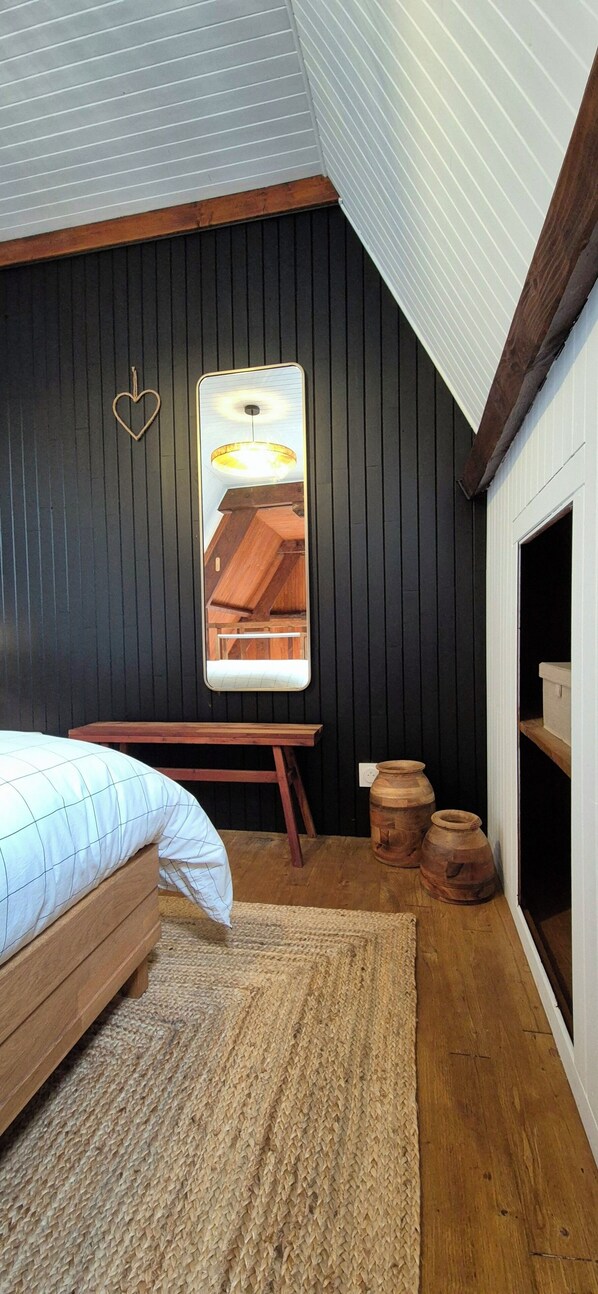 A bedroom with a sloped ceiling, wooden bed, a large mirror, and a small wooden table. - Cozy house in the heart of the Bastide with private courtyard and closed garage (Domme)
