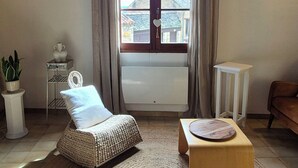 A cozy living room with a large window, a woven chair, a small wooden stool, and a potted plant. - Cozy house in the heart of the Bastide with private courtyard and closed garage (Domme)