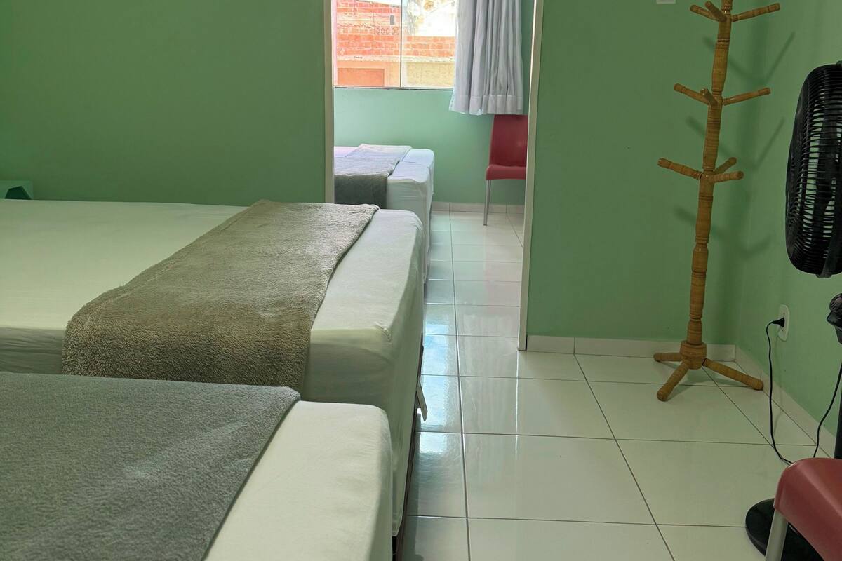 A hotel room with two beds, a wooden coat rack, a red chair, and a fan.