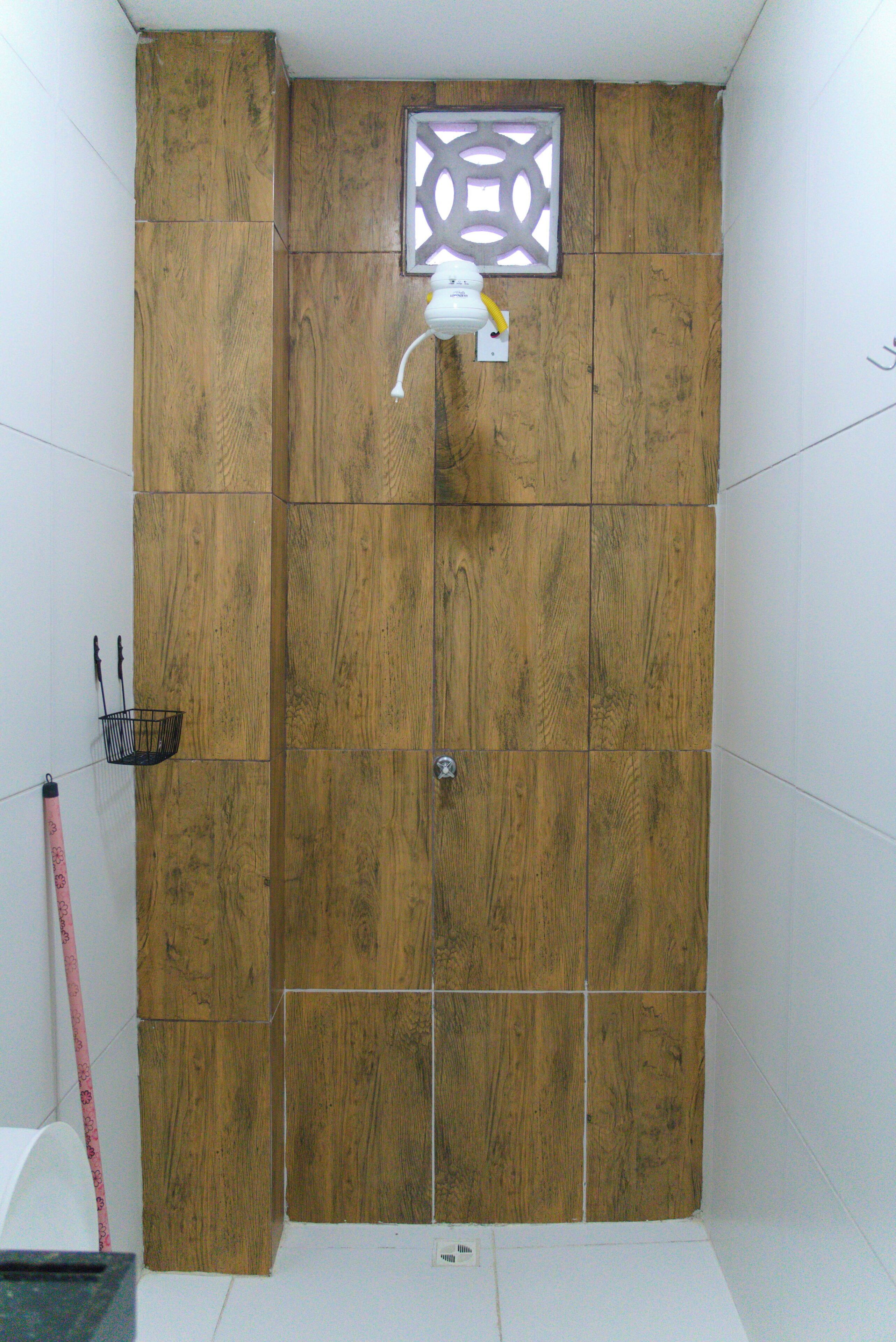 Een badkamer met houten lambrisering, een douche en een klein raam met een geometrisch ontwerp.