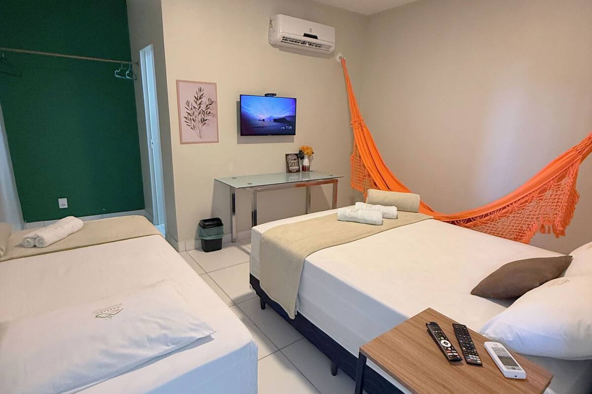 A hotel room with two beds, a TV, an air conditioner, a small table with remote controls, and a hammock.