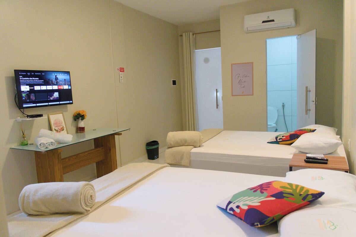 A hotel room with two beds, a TV, a desk with a computer, and a bathroom door.