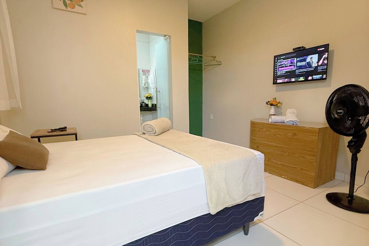 A bedroom with a bed, a dresser, a TV, and a fan.