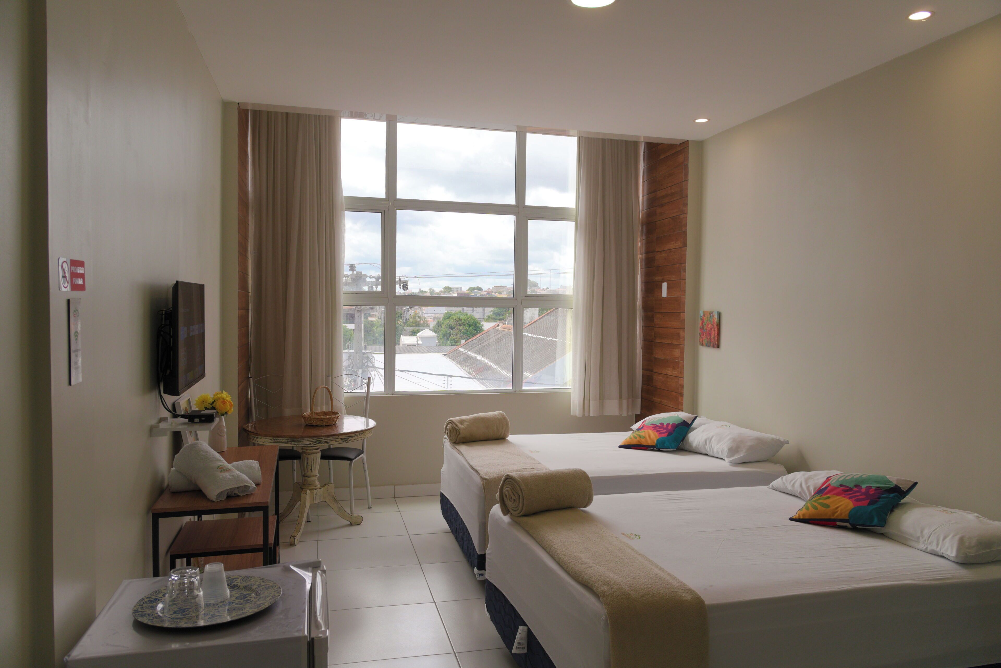 A hotel room with two beds, a small table with a chair, a TV, and a window with a view of the city.
