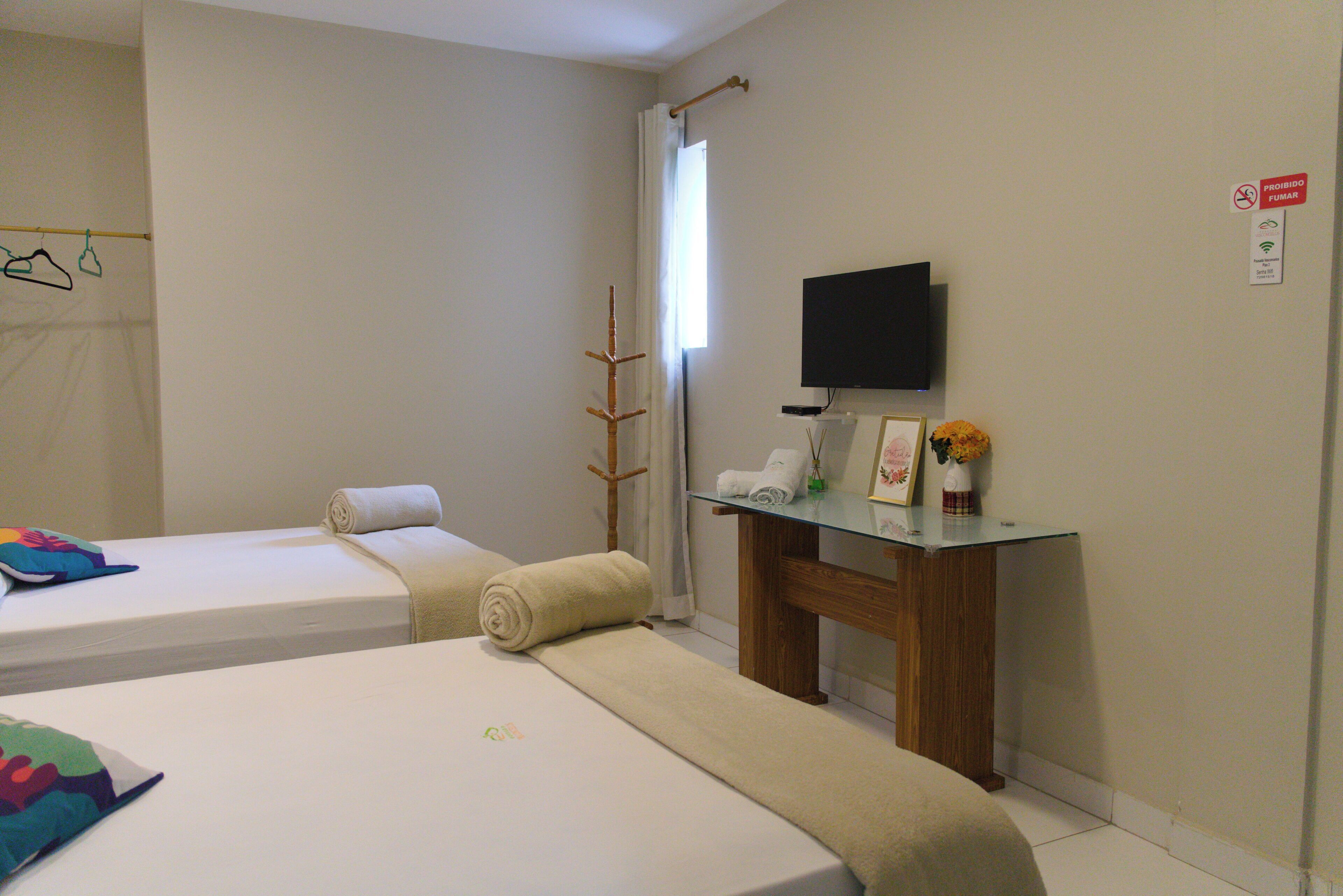 A hotel room with two beds, a TV, a small table with a vase, and a 'no smoking' sign.