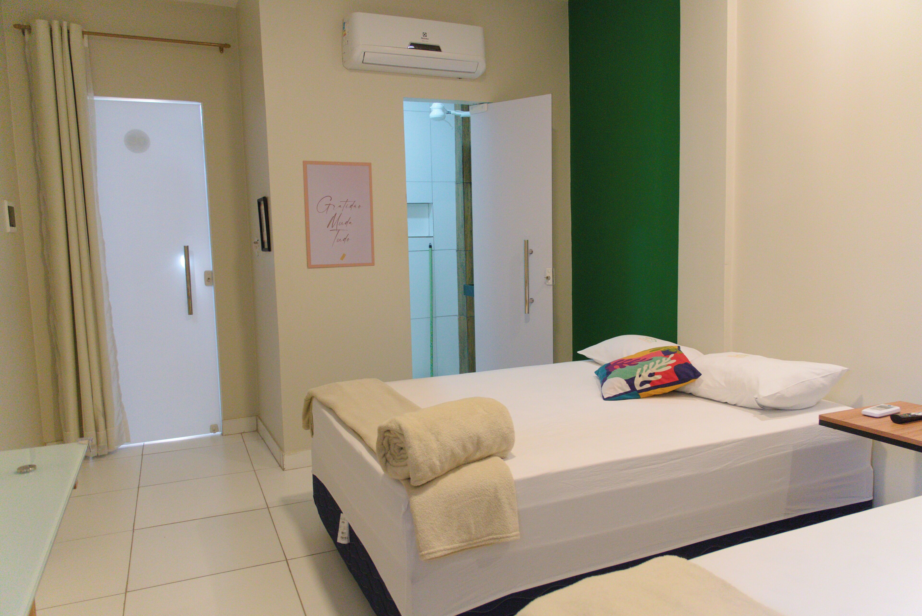 Ein Hotelzimmer mit einem Bett, einem Nachttisch, einer Wand-Klimaanlage und einer Tür zu einem anderen Raum.