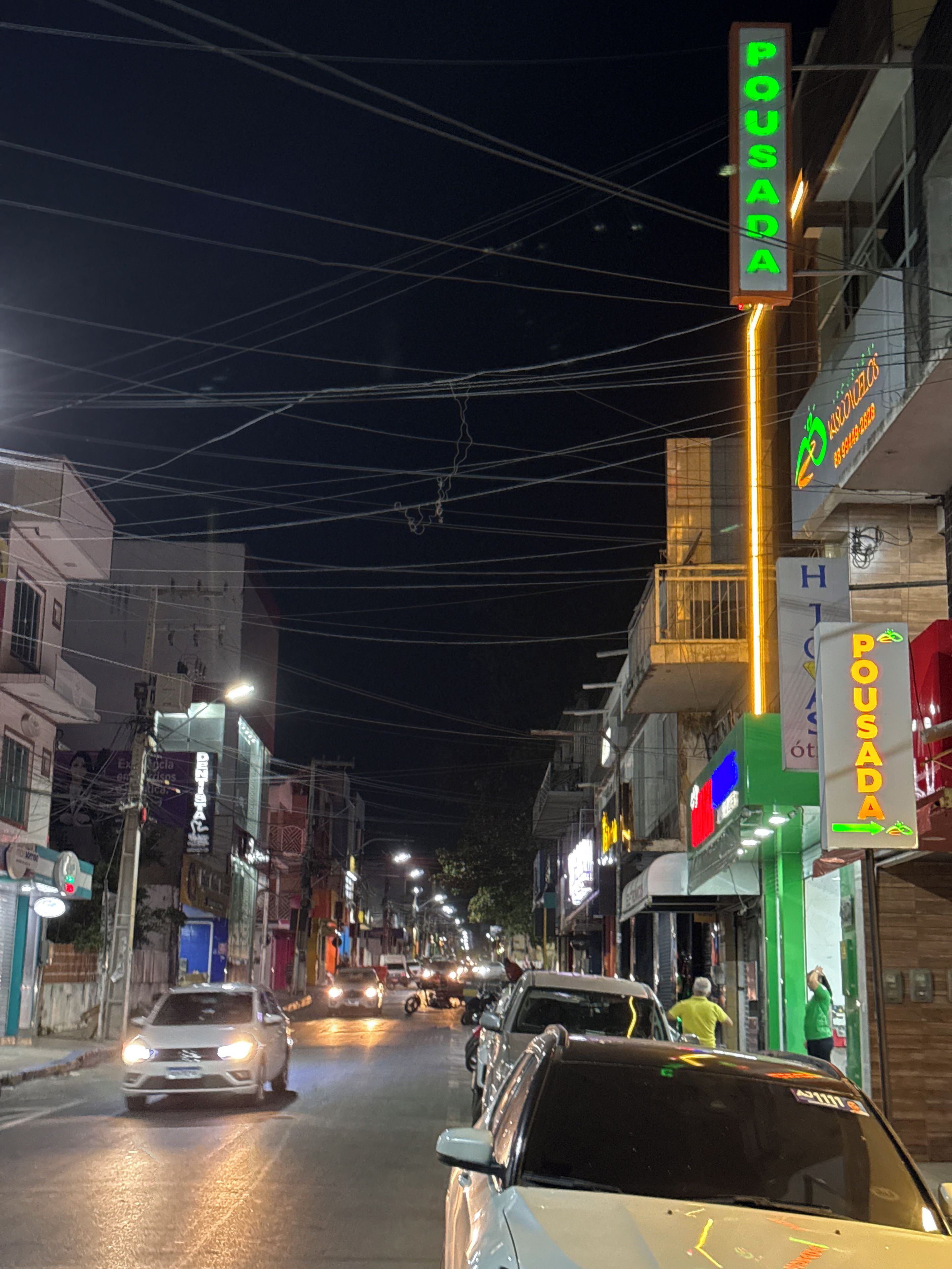 A nighttime street scene with illuminated signs and vehicles.