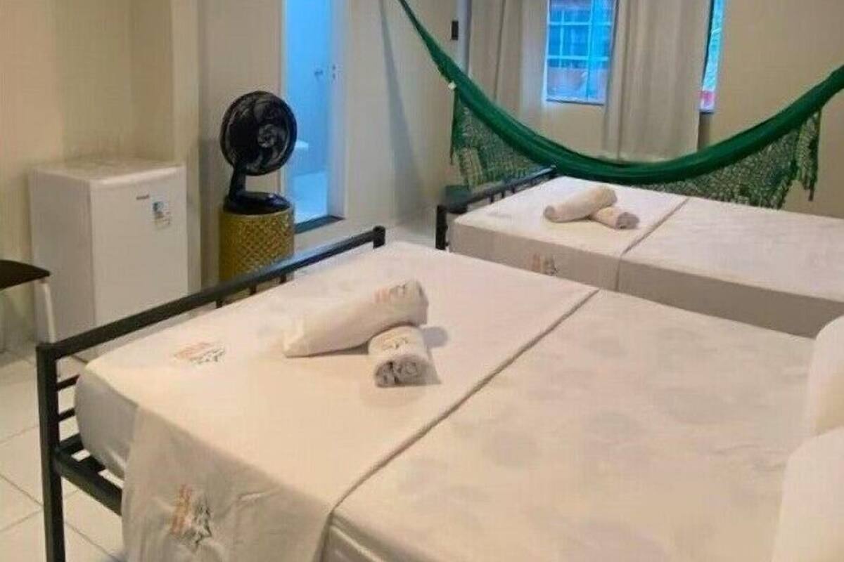 A hotel room with two beds, a small table, a fan, and a hammock.