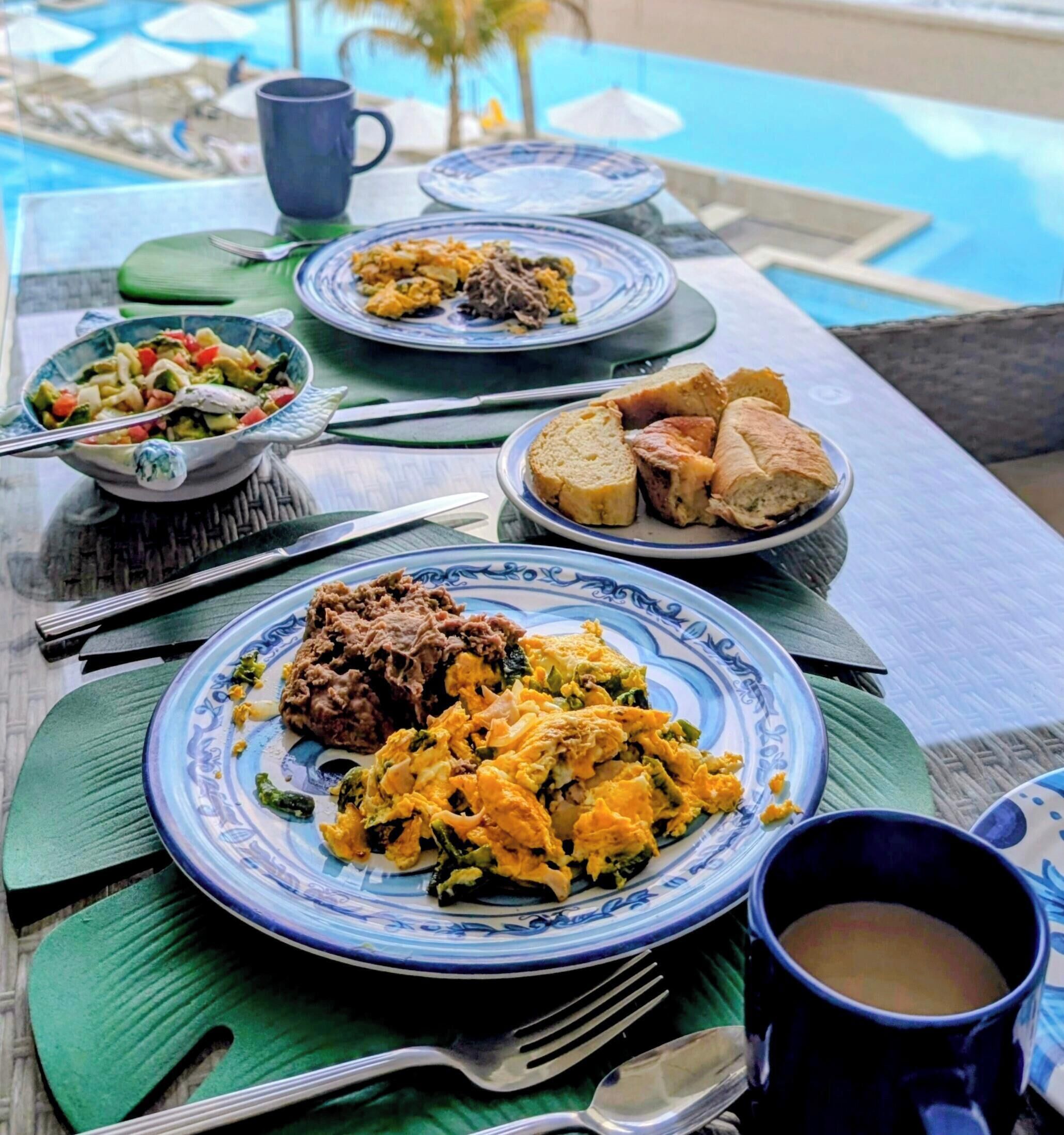 A table set with breakfast dishes, a coffee cup, and a view of the ocean.