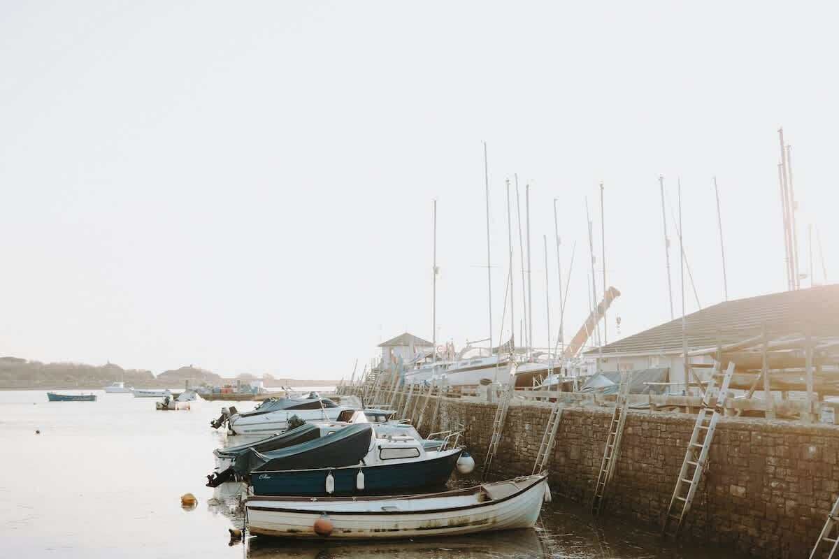 A marina with boats docked, a stone wall, and a building with a sloped roof.