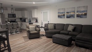 A modern living room with a sectional sofa, a small armchair, and a dining area with a kitchen in the background. - Located in the Eli community of Russell Springs near Beautiful Lake Cumberland. (Russell Springs)