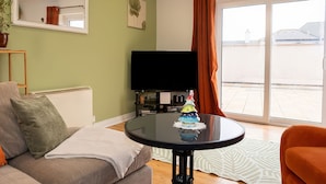 Ein Wohnzimmer mit einer Couch, einem Couchtisch, einem Flachbildfernseher und einem großen Fenster mit Vorhängen.