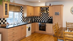 Eine kleine Küche mit Holzschränken, einer schwarz-weißen Schachbrettfliesenrückwand, einem eingebauten Ofen und einem Essbereich mit Holztisch und -stühlen.