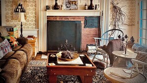 A cozy living room with a fireplace, a sofa, a coffee table, and various decorative items. - Rustic 5-Bedroom Home on 140 Acres perfect for White Mountain family getaways (Campton)
