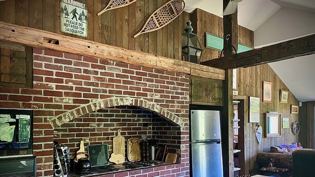 A kitchen with a brick fireplace, a refrigerator, and wooden beams. - Rustic 5-Bedroom Home on 140 Acres perfect for White Mountain family getaways (Campton)