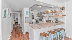 A modern kitchen with a central island, bar stools, and a dining area. - Direct Oceanfront 3BR/3BA | Upgraded Condo w/ Pool (North Myrtle Beach)