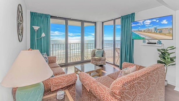 A spacious balcony with a cityscape view, furnished with a sofa, armchair, and a small table. - Direct Oceanfront 3BR/3BA | Upgraded Condo w/ Pool (North Myrtle Beach)