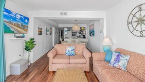 A living room with a sofa, a dining table, and a kitchen in the background. - Direct Oceanfront 3BR/3BA | Upgraded Condo w/ Pool (North Myrtle Beach)