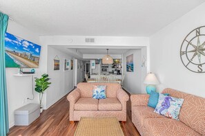 A living room with a sofa, a dining table, and a kitchen in the background. - Direct Oceanfront 3BR/3BA | Upgraded Condo w/ Pool (North Myrtle Beach)