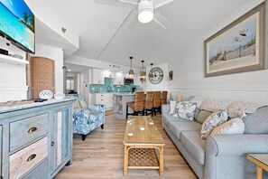 Een ruime woonkamer met een eettafel, twee banken en een keuken op de achtergrond.