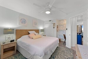 A bedroom with a large bed, a nightstand with a lamp, a ceiling fan, and a door leading to another room. - Rest Ashore | Luxury 1BR w/ Stunning Ocean Views (Myrtle Beach)
