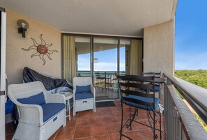 A balcony with wicker furniture, a table, and a chair. - Rest Ashore | Luxury 1BR w/ Stunning Ocean Views (Myrtle Beach)