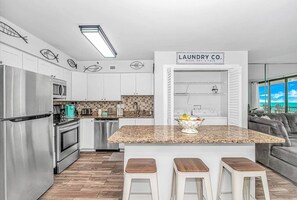 A modern kitchen with stainless steel appliances, a granite countertop, and a sign reading "LAUNDRY CO." - Oceanfront | 3BR Sleeps 8 | Indoor Pool + Views (North Myrtle Beach)