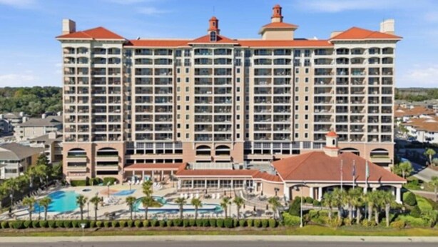 A large hotel with multiple floors, a central courtyard with a pool, and a red-roofed building. - Luxury 3BR/3BA Condo with Panoramic Ocean Views! (North Myrtle Beach)