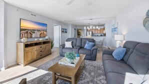 A modern living room with a grey sofa, a wooden coffee table, and a TV on the wall. - Luxury 3BR/3BA Condo with Panoramic Ocean Views! (North Myrtle Beach)