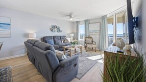 A modern living room with a grey sofa, a wooden coffee table, and a chair. There is a large window with a view of the sea. - Luxury 3BR/3BA Condo with Panoramic Ocean Views! (North Myrtle Beach)