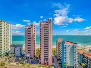 A coastal hotel complex with two prominent pink towers, a parking area, and a beach view. - Luxury Direct Oceanfront 1BR on the Boardwalk (Myrtle Beach)