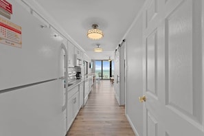A narrow hallway with white walls and wooden flooring leading to a balcony with a view. - Luxury Direct Oceanfront 1BR on the Boardwalk (Myrtle Beach)