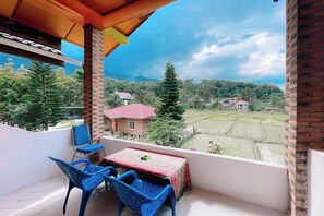 A balcony with a table and chairs, overlooking a rural landscape with fields and houses. - Doni Guest House by Staigo (Samosir)